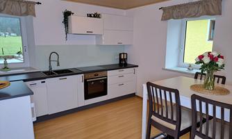 A modern kitchen interior with bright wooden flooring and stylish furniture. There is a dining table with chairs and a well-equipped kitchenette.