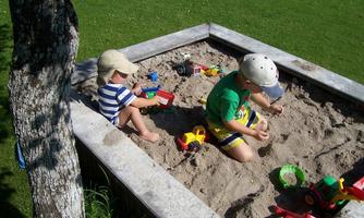 Two children are playing in the sandbox. They are using different toys and having a lot of fun outdoors.