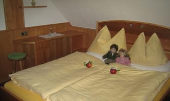 A cozy bedroom with a large bed and wooden shelves. On the bed sit two dolls with red apples.