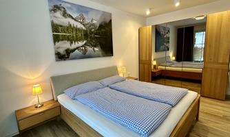 A cozy bedroom with a double bed and wooden furniture. A large picture of a mountain landscape hangs on the wall.