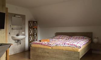 A cozy bedroom with a large bed and a modern sink. The walls are light, and the room has wooden furniture for a warm atmosphere.