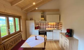 A cozy kitchen with wooden furniture and large windows. The room has a friendly, bright atmosphere with modern appliances.
