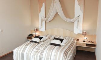 An elegant bedroom with a large bed and striped bed covers. The walls are in neutral colors, and there are two nightstands with lamps.