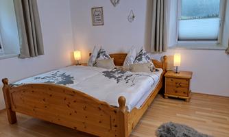 A cozy bedroom with a wooden bed and elegant pillows. The room has bright colors and large windows that let in natural light.