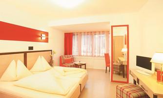A modern hotel room with a double bed and a beautiful view from the window. The decor is bright and friendly, with a table and a chair.