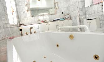 An elegant bathroom with a white bathtub and marbleized walls. In the background, there is a large mirror and some bathroom furniture visible.