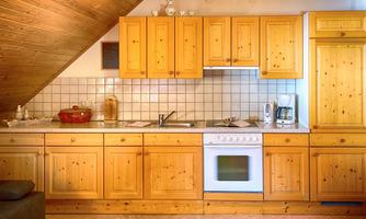 A cozy kitchen with wooden cabinets and a sloping roof. The equipment includes a stove, a sink, and various kitchen utensils.