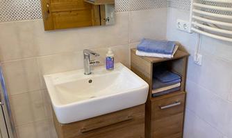 A modern bathroom with wooden details and an elegant sink installation. The floor is designed with colorful tiles in blue, orange, and beige.