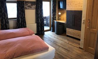 A cozy bedroom with two single beds and checked bedcovers. The room has wooden flooring and a desk, as well as large windows with a view outside.