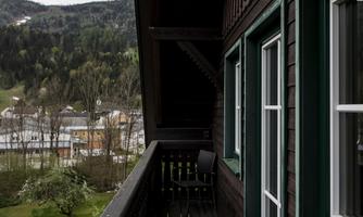 A balcony with a chair and a view of a green landscape. In the background, houses and mountains can be seen.