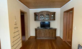 A cozy living space with a wooden floor and a wooden ceiling. The decor includes a TV unit and a sofa, with a small Christmas tree decoration on the wall.