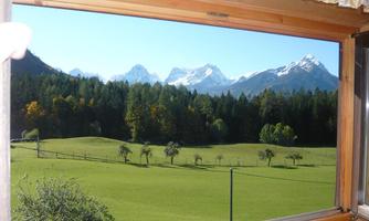 A beautiful view from the window of a green meadow with trees and snow-capped mountains in the background. The sky is clear and nature is calm.