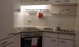 A modern kitchen with white cabinets and a green doormat. There are appliances such as a stove and a sink.