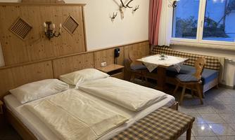 A cozy room with a double bed, a seating area, and wooden decor. There is a window with an outdoor view and a warm atmosphere.