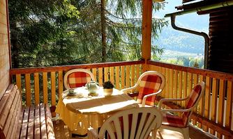 A cozy balcony with a wooden railing and a view of nature. Two chairs and a table are lovingly set.
