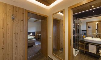 A cozy room with wooden paneling and two doors. On the left, there is a bedroom, and on the right, there is a modern bathroom with a shower.