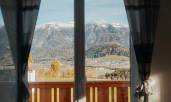 A view from a window onto a picturesque mountain landscape with snow-covered peaks. The scene is peaceful and showcases the beauty of nature.