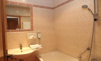 A bright bathroom with a bathtub and a sink. The walls are tiled and there is a mirror above the sink.