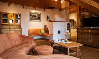 A cozy living space with a large orange sofa and a wooden table. The warm wood tones and bright light create an inviting atmosphere.
