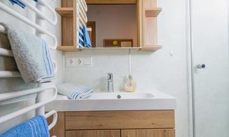 A modern bathroom with a wooden sink and a large mirror. Towels in blue are neatly hanging on a towel rack.