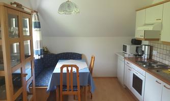 A cozy kitchen with a dining area and a window. The table is set with a blue cloth, and the furniture is light and modern.