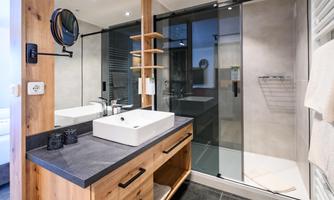 A modern bathroom with wood and stone elements. It features a sink unit, a shower with a glass partition, and stylish lighting.