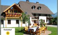A cozy yard with a large wooden house and several flower balconies. People sit at the outdoor table and enjoy time together.