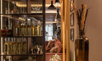 A modern room with an elegant shelf displaying various bottles and glasses. In the foreground, there is a stylish vase with decorative elements.