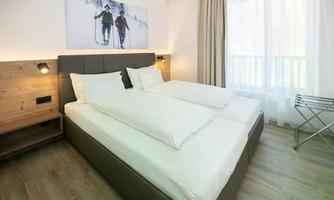 A modern bedroom with two single beds and large windows. A picture of skiers in a winter landscape hangs on the wall.