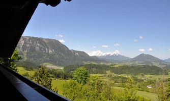 A picturesque landscape with high mountains and green forests. In the background, snow-capped peaks can be seen.