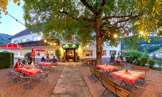 A cozy restaurant with terrace seating under a large tree. The tables are decorated and there is a relaxed atmosphere.