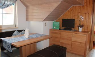 A cozy living space with a wooden table and chairs. A television and a floral decoration are on the wall.
