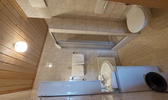 A simple bathroom with a shower, a sink, and a toilet. The walls are tiled in light colors and the ceiling is made of wood.