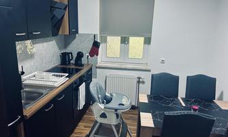 A modern kitchen with wooden and black cabinets. A dining table with chairs and a high chair are also available.