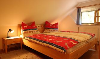 A cozy bedroom with a wooden bed and colorful pillows. Next to the bed is a nightstand with a lamp.