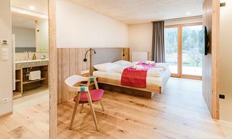 A modern hotel room with a comfortable bed and a spacious window front. The wooden floor and minimalist decor create an inviting atmosphere.