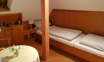 A cozy room with two single beds and wooden shelves. The room is bright and simply furnished with a small table.