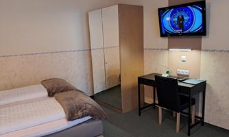 A simple, modern hotel room with two beds, a desk, and a TV on the wall. The room has a wardrobe and is decorated in bright colors.