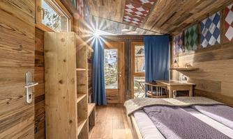 A cozy room with wooden paneling, large windows, and a table. The warming sun shines through the windows, creating an inviting atmosphere.