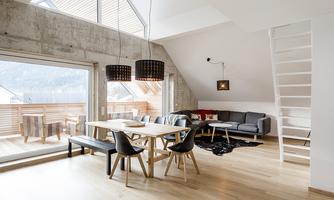 A modern, bright living room with a cozy seating area and a dining area. Large windows provide plenty of daylight and a view outside.