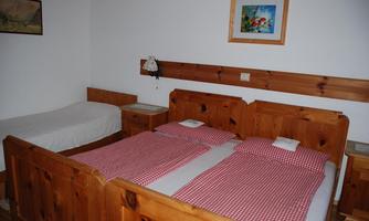 A simple bedroom with two wooden beds and checkered bedding. A colorful picture hangs on the wall, and there is a nightstand next to the beds.