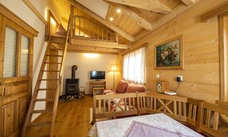 A cozy wooden cabin with an elevated sleeping area and a living area. The large windows let in plenty of light and create an inviting atmosphere.