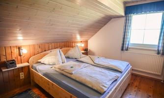 A cozy bedroom with a double bed and wood paneling. The window lets in plenty of daylight and creates a pleasant atmosphere.