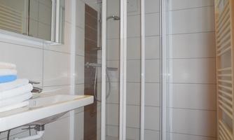 A modern bathroom with a shower cabin and a sink. Clean tiles and towels are visible.