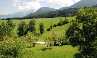 A picturesque landscape with green meadows and gentle hills. In the background, there are mountains and a blue sky.