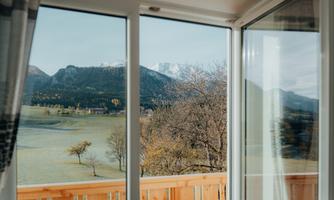 A view through large windows of a picturesque landscape with mountains and trees. The sky is clear and nature radiates tranquility.