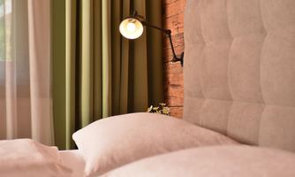 A cozy bedroom with a padded headboard and two pillows. The green curtains and soft light create a relaxed atmosphere.