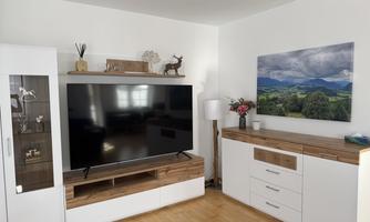 A modern living room with a large television and a wooden dresser. A landscape painting of mountains and clouds hangs on the wall.