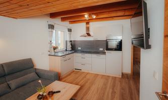 A modern kitchenette with wooden shelves and a cozy seating area. Plenty of daylight streams through the window into the room.
