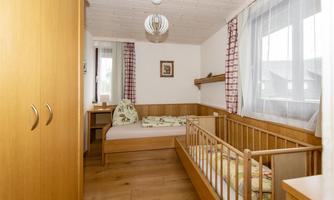 A cozy children's room with a wooden bed and a cot. Bright walls and large windows create a friendly atmosphere.